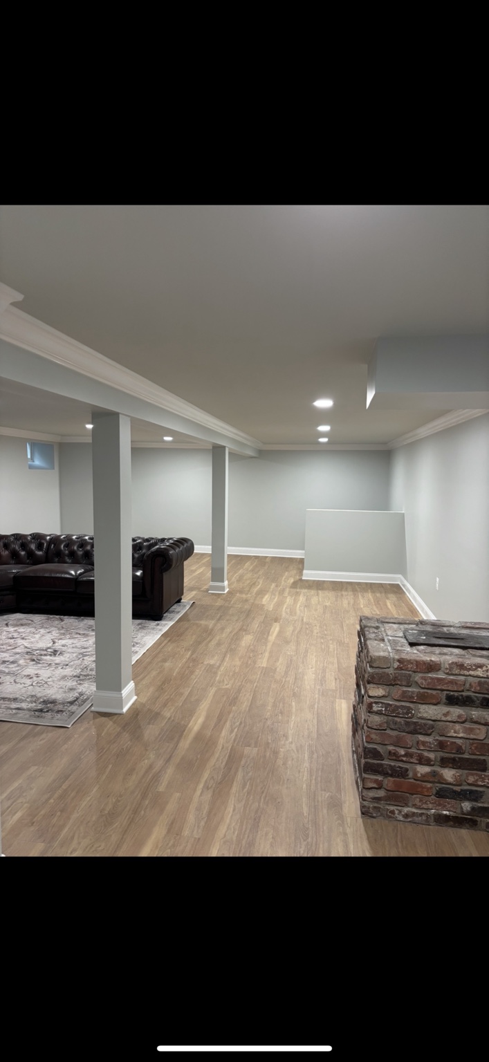Finished basement with wood-look flooring, recessed lighting and trimmed support columns