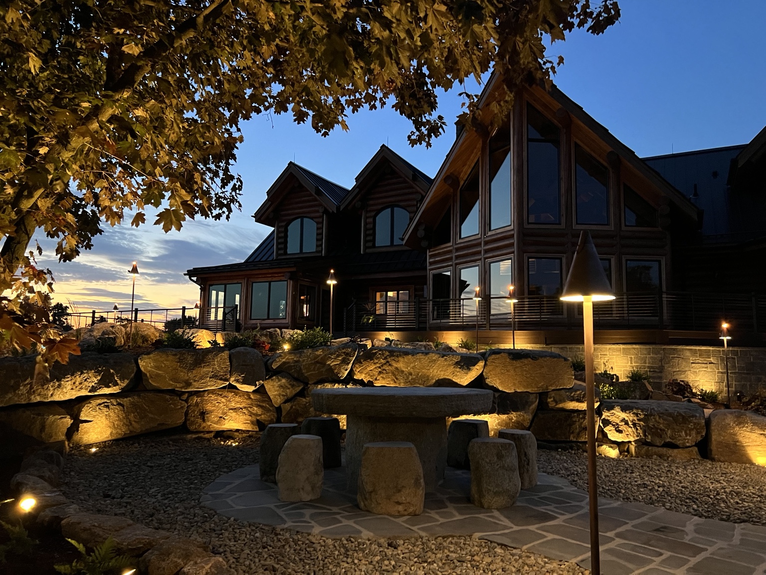 Boulder landscape, stone seating and illuminated home at dusk