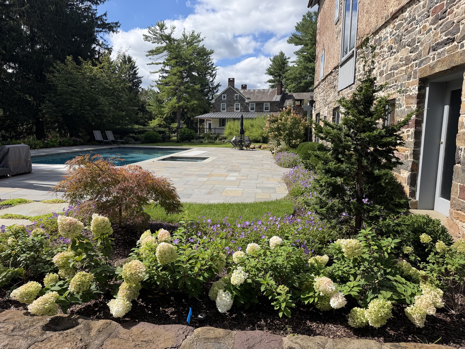 Layered flowering beds beside a pool and stone home